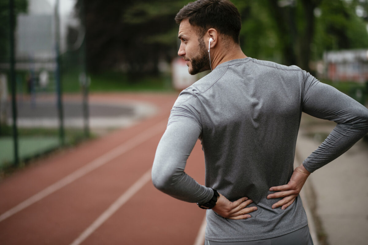 Sportsman suffering from backache at park outdoors. Back Pain. Sport injury