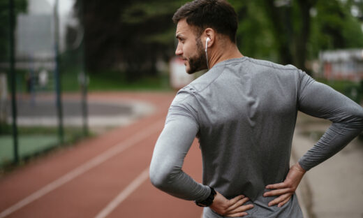 Sportsman suffering from backache at park outdoors. Back Pain. Sport injury