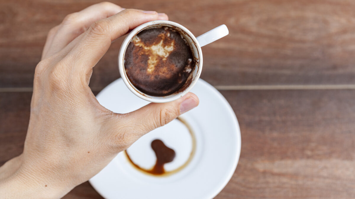 A caucasian woman is performing fortune reading ( kahve fali ) using leftover coffe grounds in ceramic Turkish coffe cup. A popular activity in Turkey. Coffee drops form shapes and patterns.