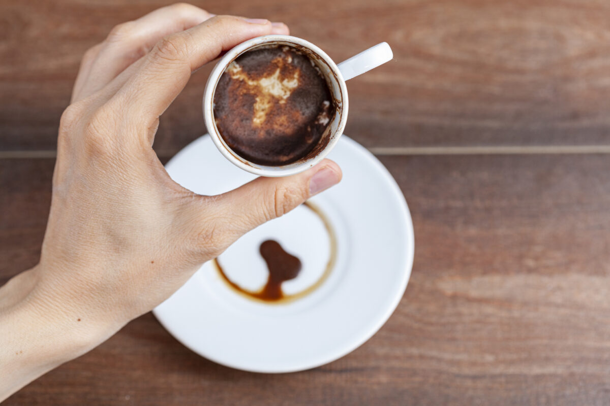 A caucasian woman is performing fortune reading ( kahve fali ) using leftover coffe grounds in ceramic Turkish coffe cup. A popular activity in Turkey. Coffee drops form shapes and patterns.