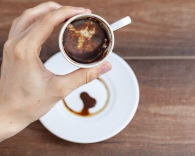 A caucasian woman is performing fortune reading ( kahve fali ) using leftover coffe grounds in ceramic Turkish coffe cup. A popular activity in Turkey. Coffee drops form shapes and patterns.