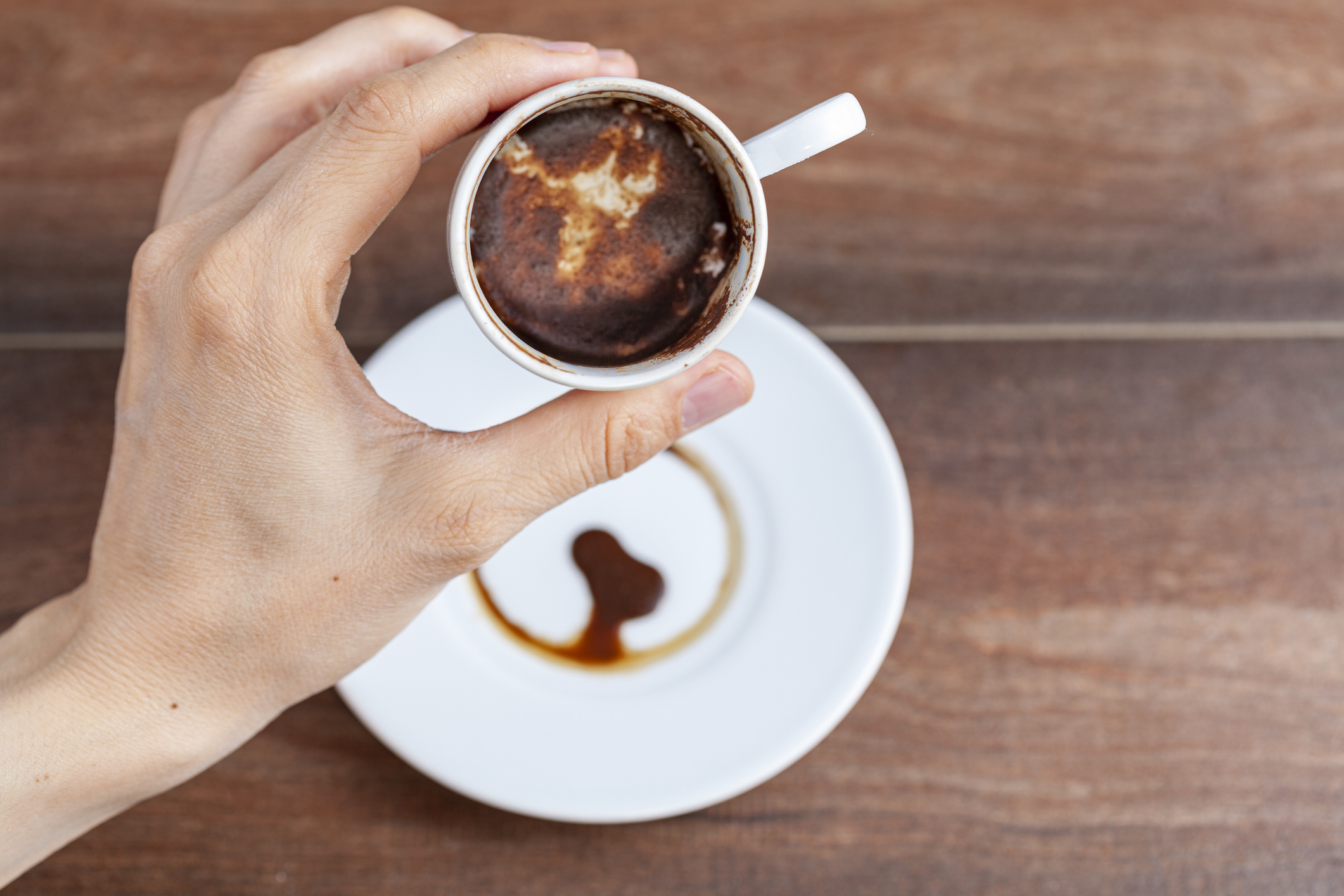 A caucasian woman is performing fortune reading ( kahve fali ) using leftover coffe grounds in ceramic Turkish coffe cup. A popular activity in Turkey. Coffee drops form shapes and patterns.