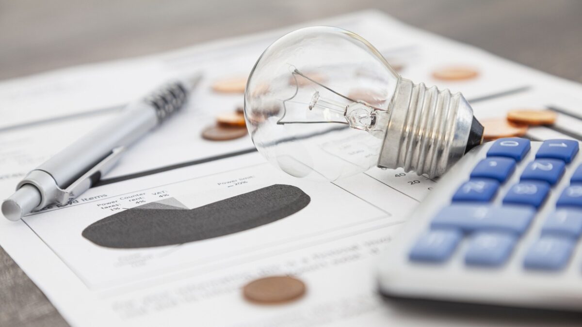 A light bulb, a pen, a calculator and some copper euro cent coins lie on top of an electricity bill