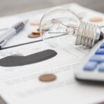 A light bulb, a pen, a calculator and some copper euro cent coins lie on top of an electricity bill