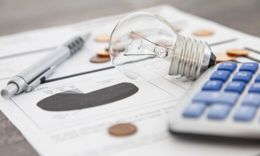 A light bulb, a pen, a calculator and some copper euro cent coins lie on top of an electricity bill