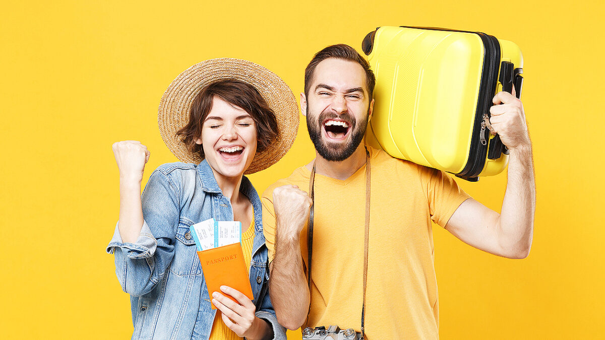 Happy young tourists couple friends guy girl isolated on yellow background. Passenger traveling abroad on weekends. Air flight journey concept. Hold passport tickets suitcase doing winner gesture