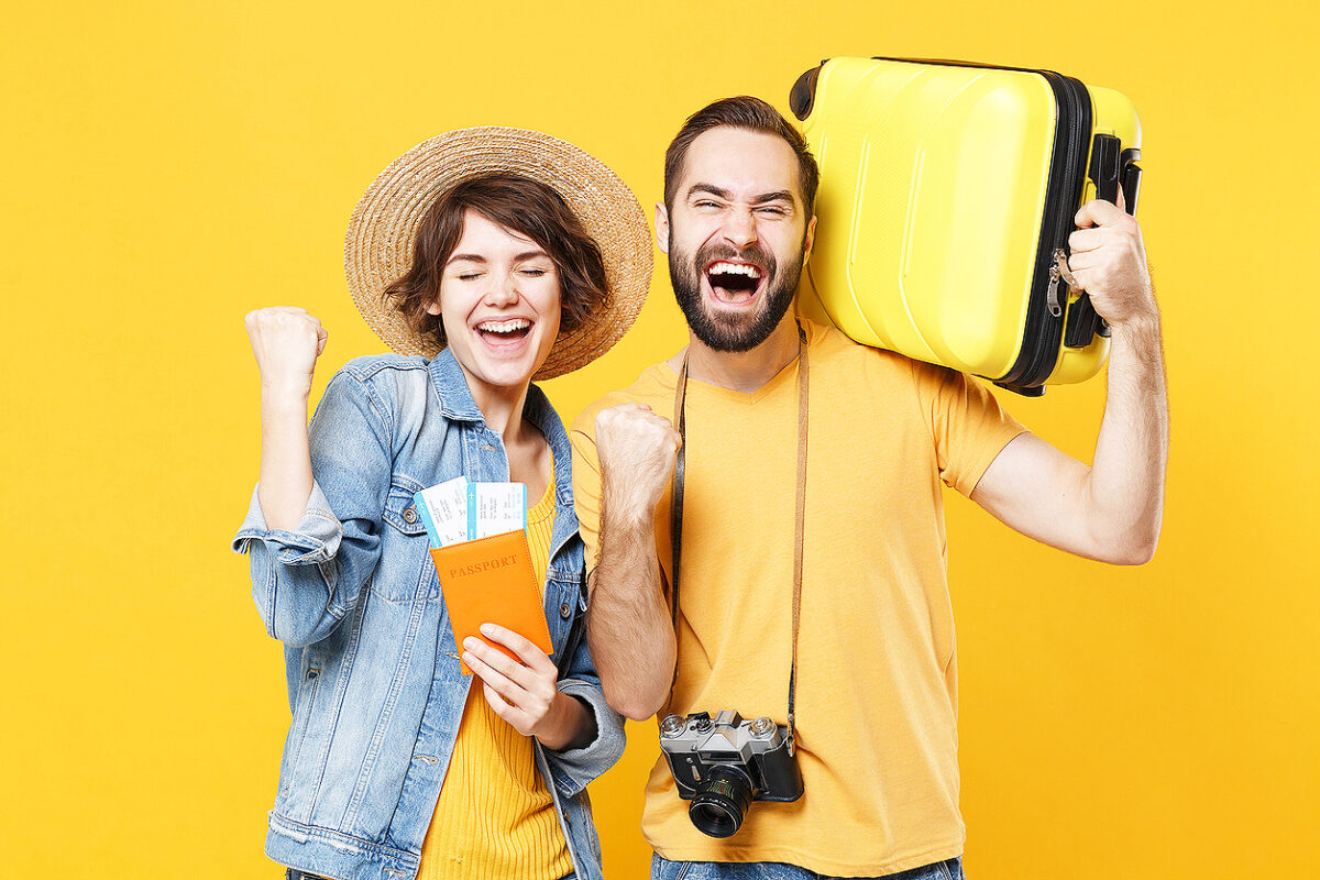 Happy young tourists couple friends guy girl isolated on yellow background. Passenger traveling abroad on weekends. Air flight journey concept. Hold passport tickets suitcase doing winner gesture