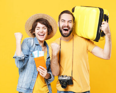 Happy young tourists couple friends guy girl isolated on yellow background. Passenger traveling abroad on weekends. Air flight journey concept. Hold passport tickets suitcase doing winner gesture