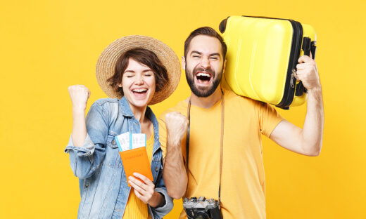 Happy young tourists couple friends guy girl isolated on yellow background. Passenger traveling abroad on weekends. Air flight journey concept. Hold passport tickets suitcase doing winner gesture