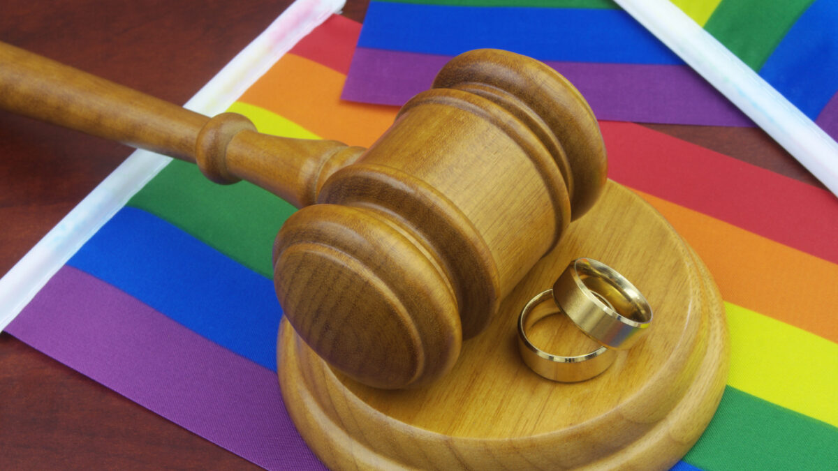 LGBT marriage, equality and laws concept. Wedding rings, wooden gavel and LGBT flags