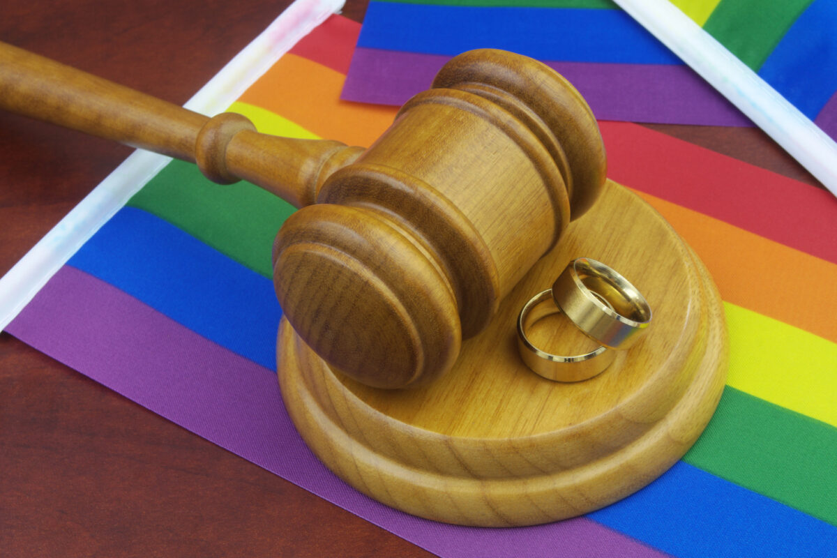 LGBT marriage, equality and laws concept. Wedding rings, wooden gavel and LGBT flags