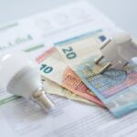 A white electric cap, a light bulb and euro banknotes on an electric bill