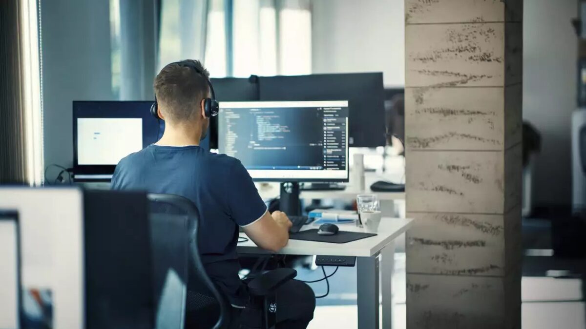 Closeup rear view of a young man coding on multiple computers