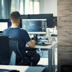 Closeup rear view of a young man coding on multiple computers