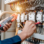 Electrician engineer uses a multimeter to test the electrical installation and power line current in an electrical system control cabinet