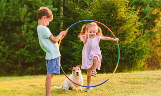 Children playing with pet dog jumping through hula hoop
