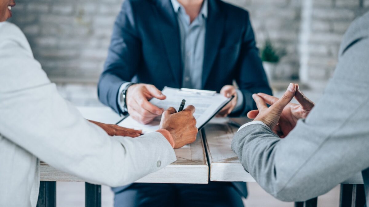 Couple sitting at desk in the bank and signing loan agreement. Shot of three business persons filling in paperwork in an office. Business persons signing a document in board room