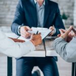 Couple sitting at desk in the bank and signing loan agreement. Shot of three business persons filling in paperwork in an office. Business persons signing a document in board room