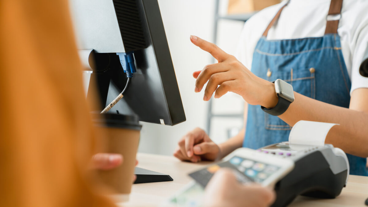 Woman cashier wears an apron and using pos terminal to payment for credit card on coffee shop counter