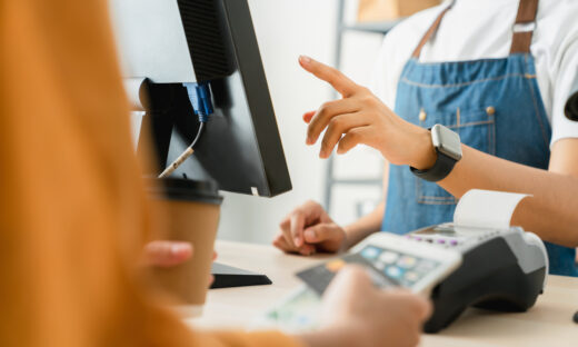 Woman cashier wears an apron and using pos terminal to payment for credit card on coffee shop counter