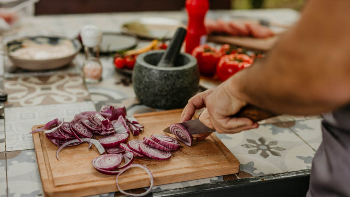A male wearing an apron cutting fresh veggies outdoors.