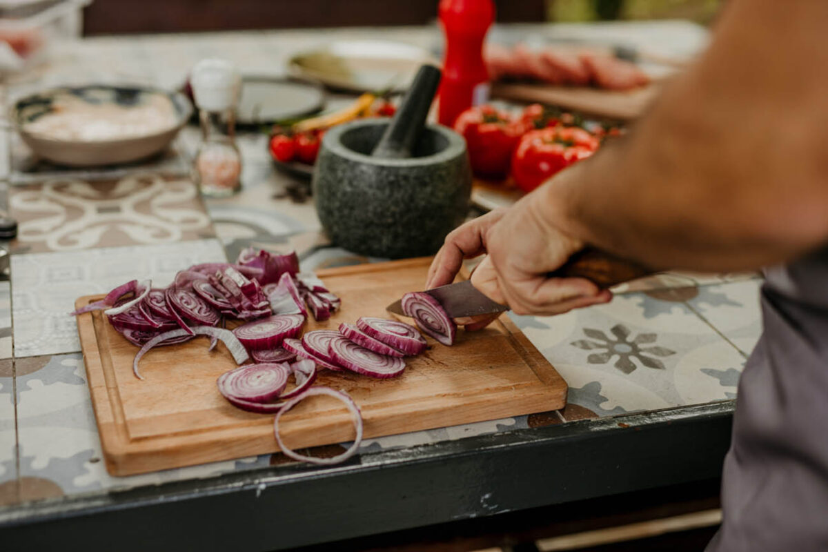 A male wearing an apron cutting fresh veggies outdoors.