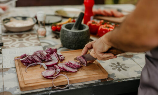 A male wearing an apron cutting fresh veggies outdoors.