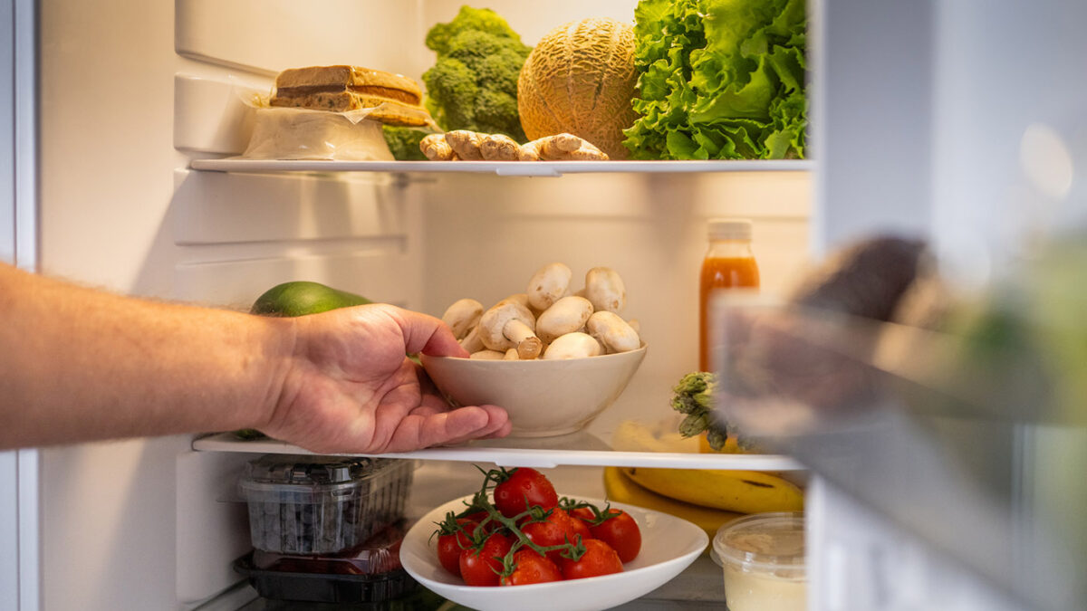 Man's hand taking out mushroom bowl from refrigerator at home.