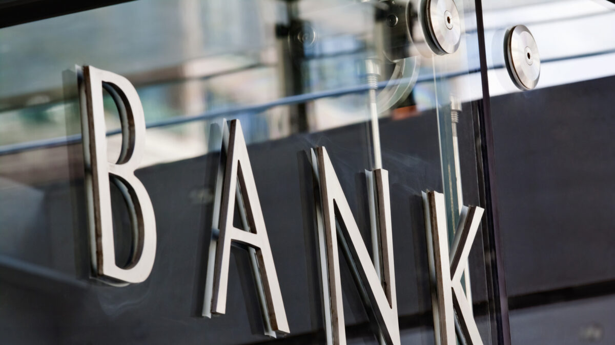 Modern metal Bank sign lettering fixed to a glass wall, with reflections in the glass