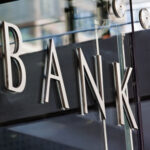 Modern metal Bank sign lettering fixed to a glass wall, with reflections in the glass