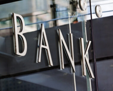 Modern metal Bank sign lettering fixed to a glass wall, with reflections in the glass