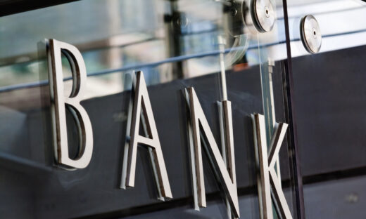 Modern metal Bank sign lettering fixed to a glass wall, with reflections in the glass