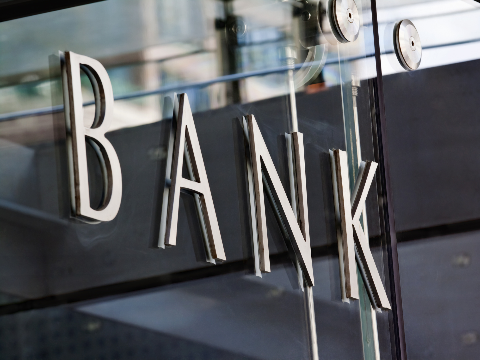 Modern metal Bank sign lettering fixed to a glass wall, with reflections in the glass