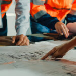 Closeup of team of industrial engineers meeting analyze machinery blueprints consult project