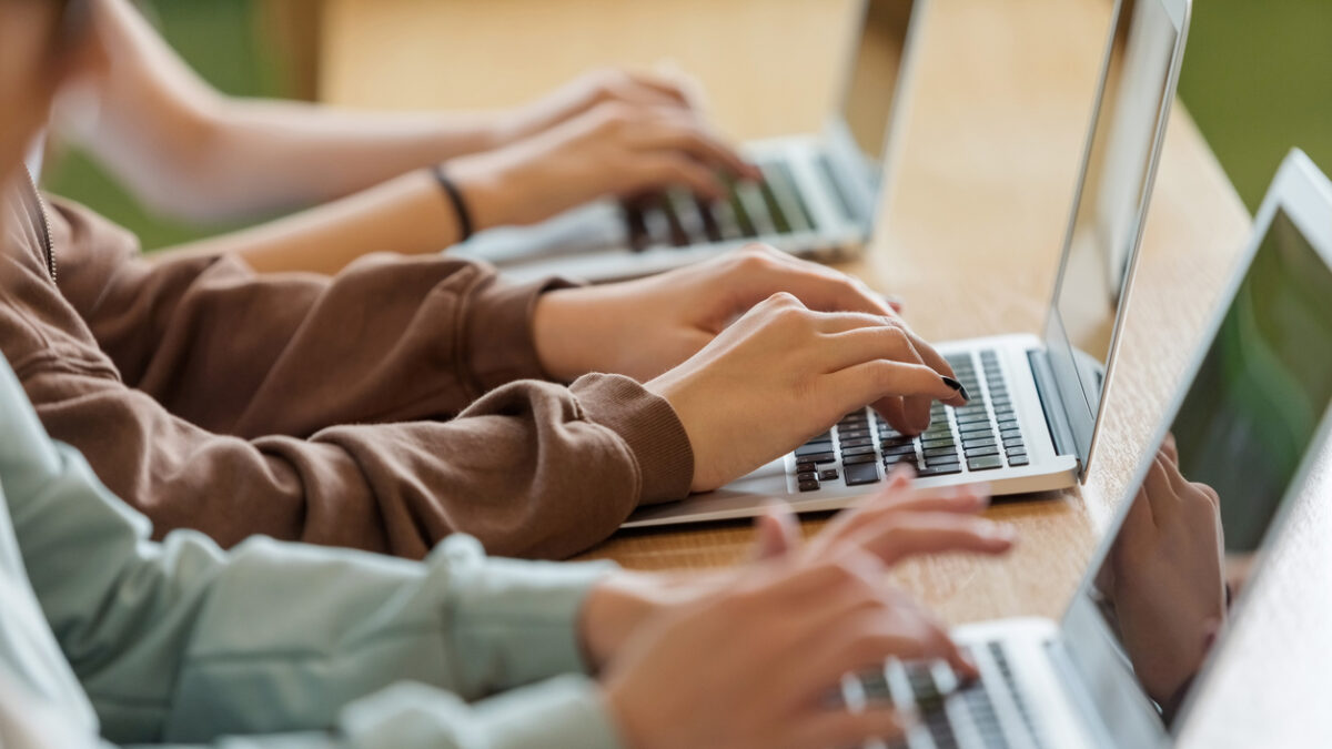 High school students sitting at the desk in the classroom during lesson, using laptops