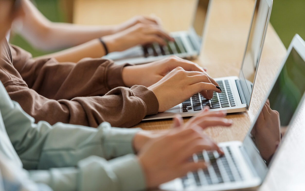 High school students sitting at the desk in the classroom during lesson, using laptops