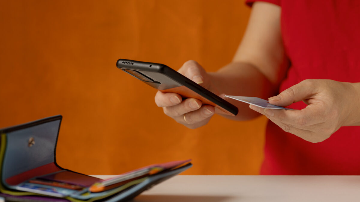 Woman's hand does a check on a bank account via a smartphone. There is a wallet with bank cards on the table