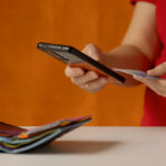 Woman's hand does a check on a bank account via a smartphone. There is a wallet with bank cards on the table