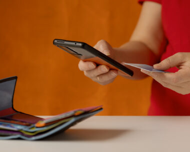 Woman's hand does a check on a bank account via a smartphone. There is a wallet with bank cards on the table