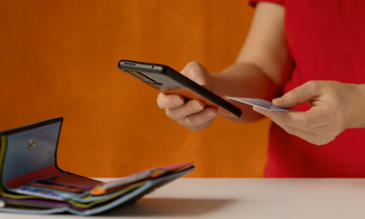 Woman's hand does a check on a bank account via a smartphone. There is a wallet with bank cards on the table