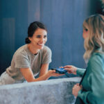 Two professional women engage in a pleasant business exchange at a stylish office. One hands a business card to another, highlighting teamwork and communication.