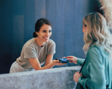 Two professional women engage in a pleasant business exchange at a stylish office. One hands a business card to another, highlighting teamwork and communication.
