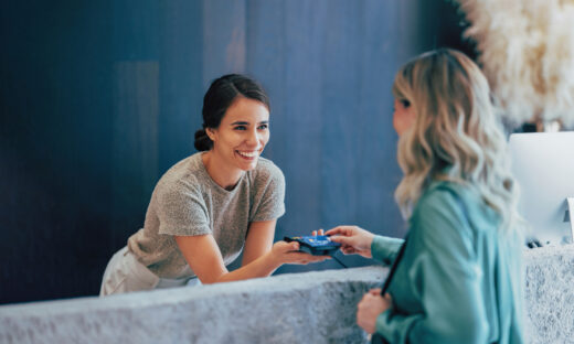 Two professional women engage in a pleasant business exchange at a stylish office. One hands a business card to another, highlighting teamwork and communication.