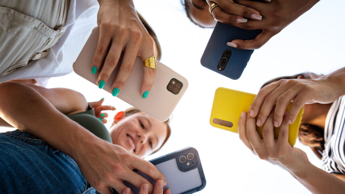 Low angle view of four female friends using phone in a circle. Focus on phones and hands. Lifestyle and technology.