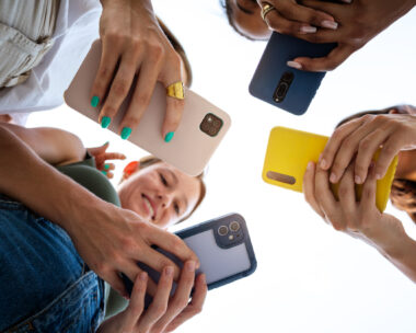 Low angle view of four female friends using phone in a circle. Focus on phones and hands. Lifestyle and technology.