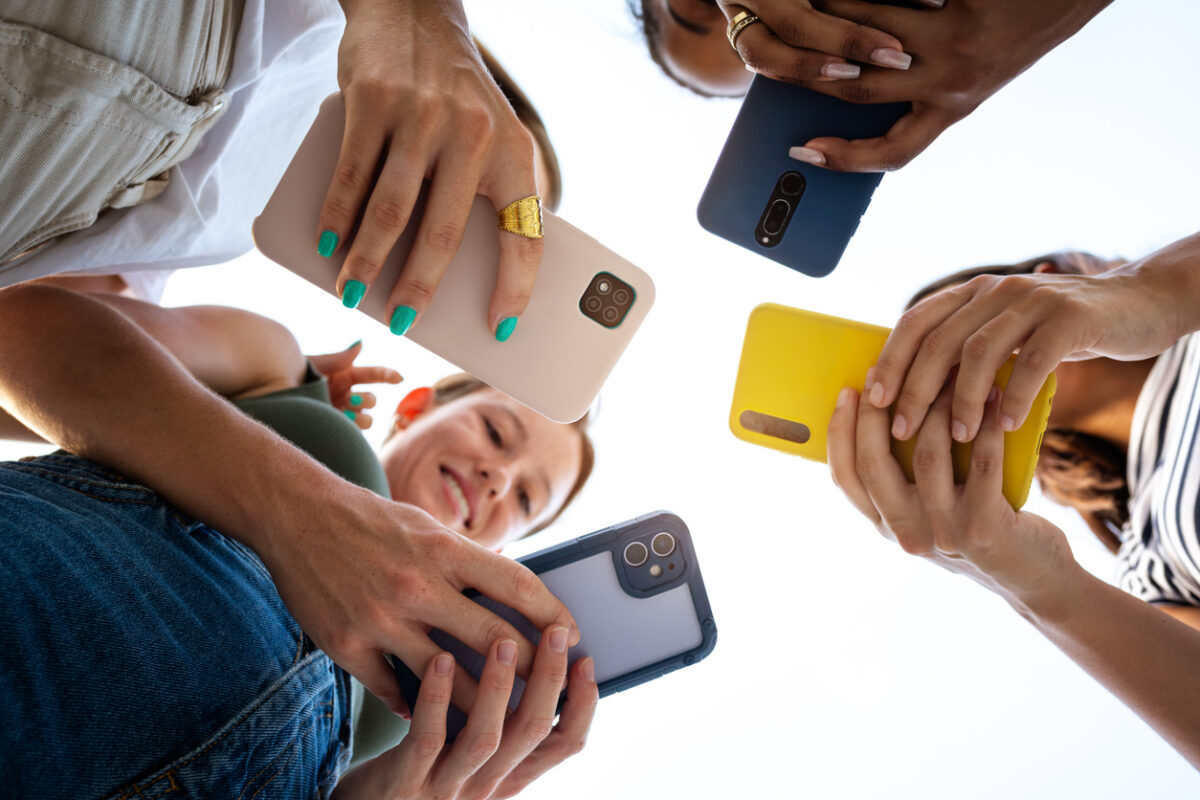 Low angle view of four female friends using phone in a circle. Focus on phones and hands. Lifestyle and technology.