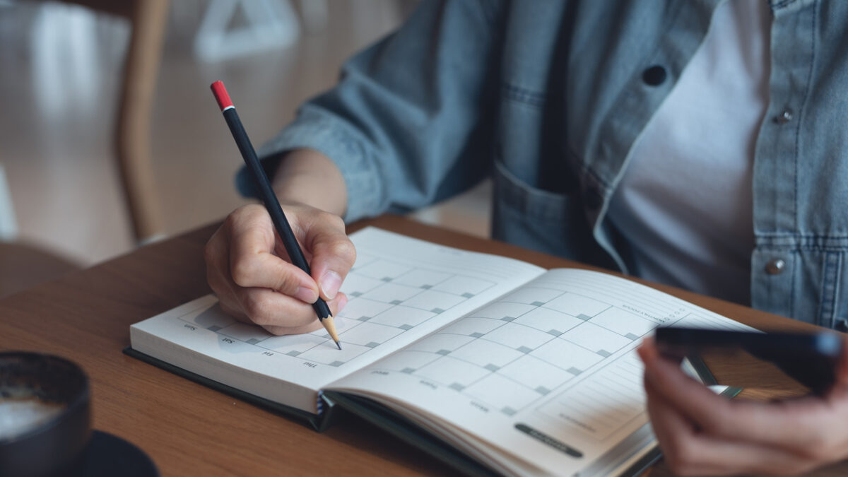 Event planner timetable agenda plan on year 2024 schedule event. Business woman checking planner on mobile phone, taking note on calendar desk on office table. Calendar event plan, work planning