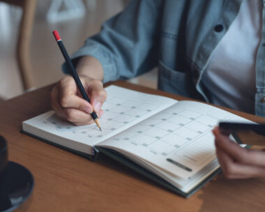 Event planner timetable agenda plan on year 2024 schedule event. Business woman checking planner on mobile phone, taking note on calendar desk on office table. Calendar event plan, work planning