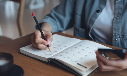 Event planner timetable agenda plan on year 2024 schedule event. Business woman checking planner on mobile phone, taking note on calendar desk on office table. Calendar event plan, work planning