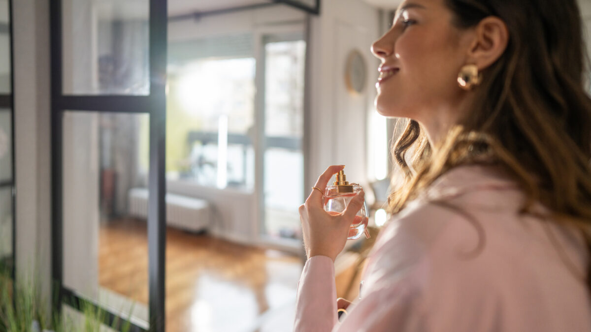 Smiling woman applying perfume in hallway while